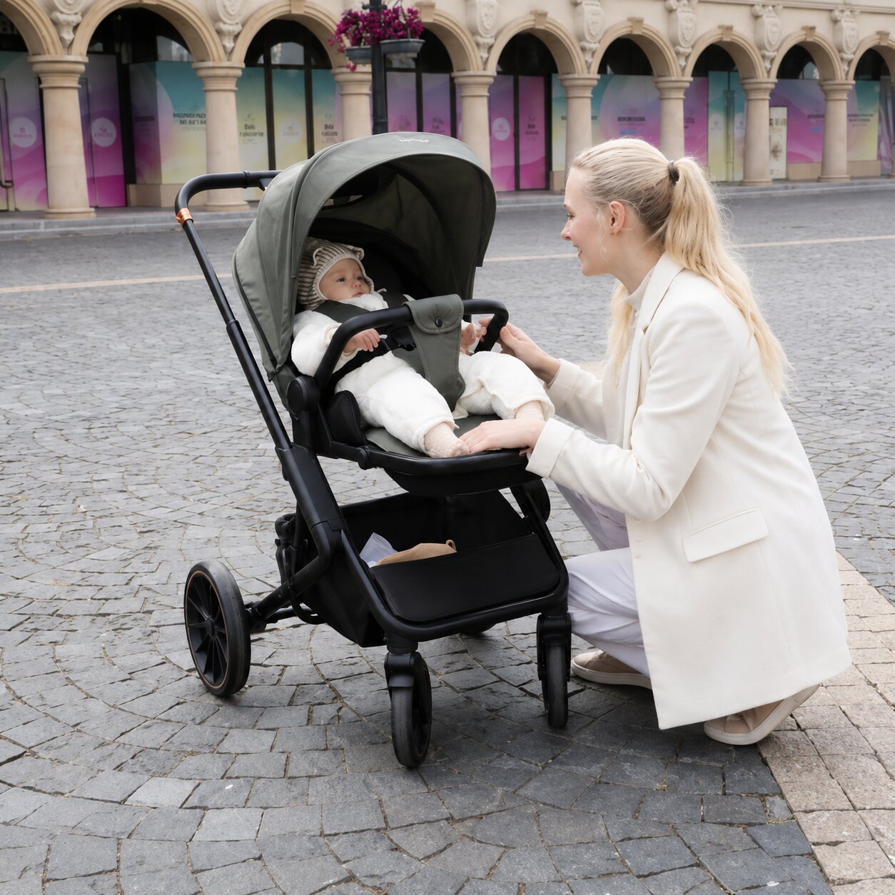 Maman accroupie devant son bebe installe dans le siege vert de la poussette BabyVoyage 4-en-1, place pavee en ville - Choupinoo