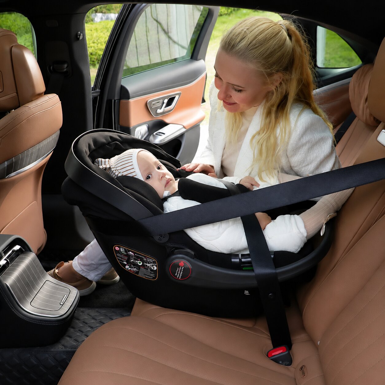 Maman blonde en veste blanche installant son bebe dans le siege auto noir de la poussette bébé BabyVoyage 2-en-1 a l'interieur d'une voiture - Choupinoo