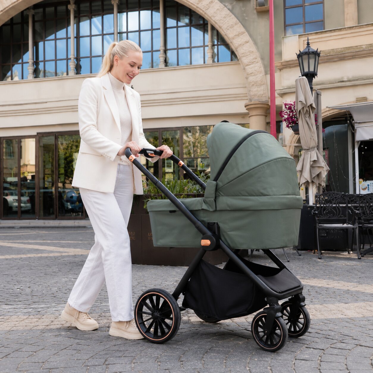 Maman en blanc poussant la poussette BabyVoyage 4-en-1 coloris vert kaki en mode nacelle, promenade en ville sur paves - Choupinoo
