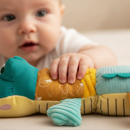 petits doigts qui pincent les segments colorés du doudou crocodile en peluche, curiosité intense
