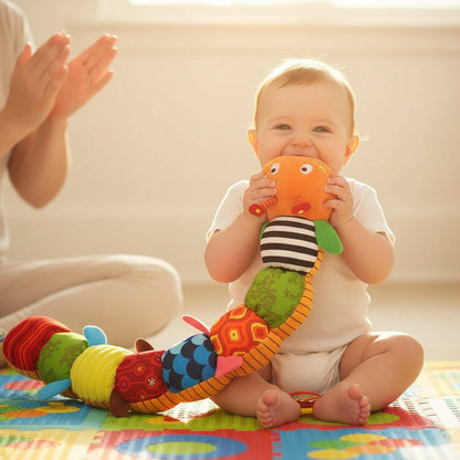 L'éclat de rire — bébé assis qui mord la tête orange de la peluche doudou chenille en riant aux éclats