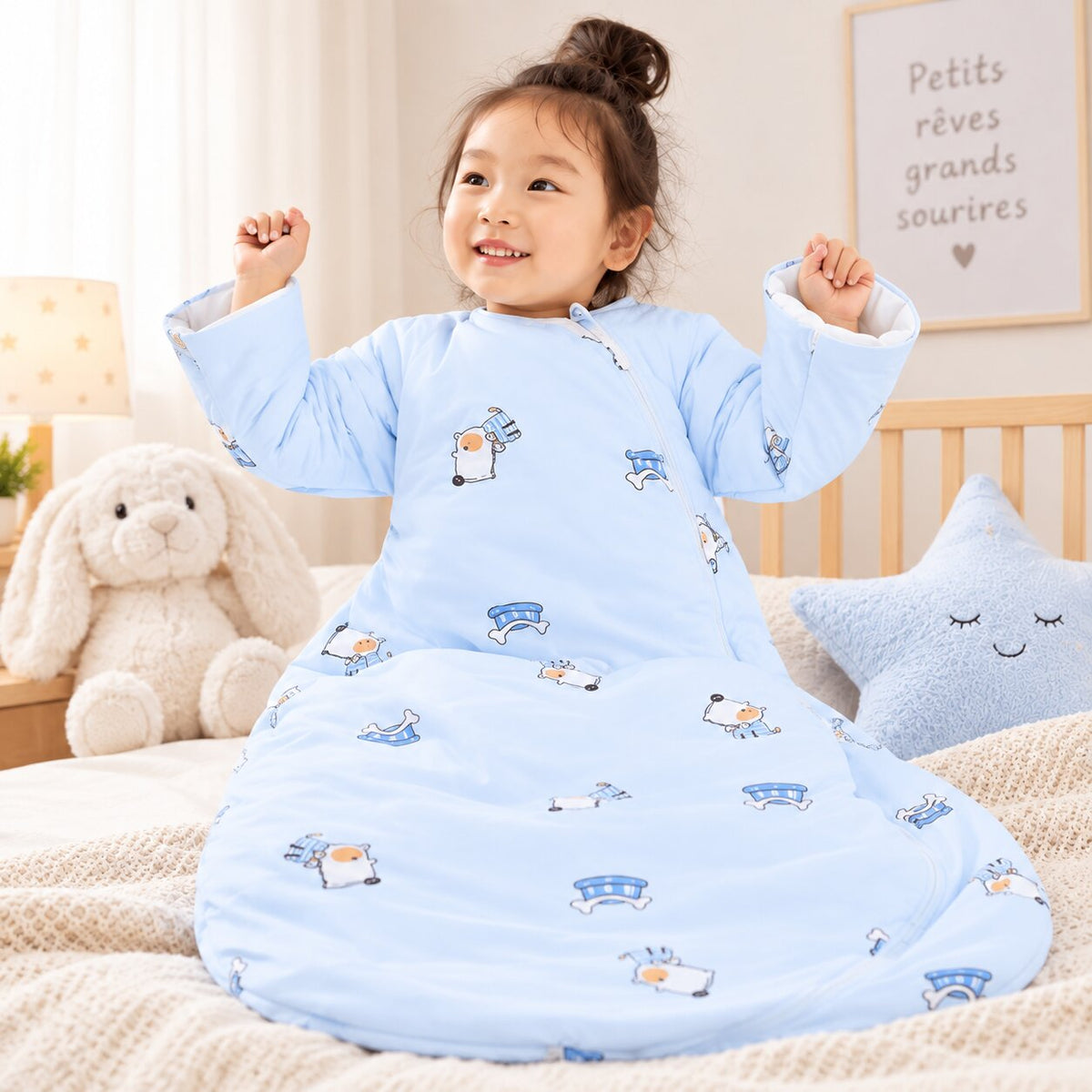 Gigoteuse évolutive bébé bleu clair à manches longues avec motifs illustrés, enfant assis sur un lit avec peluche et coussin - Choupinoo

